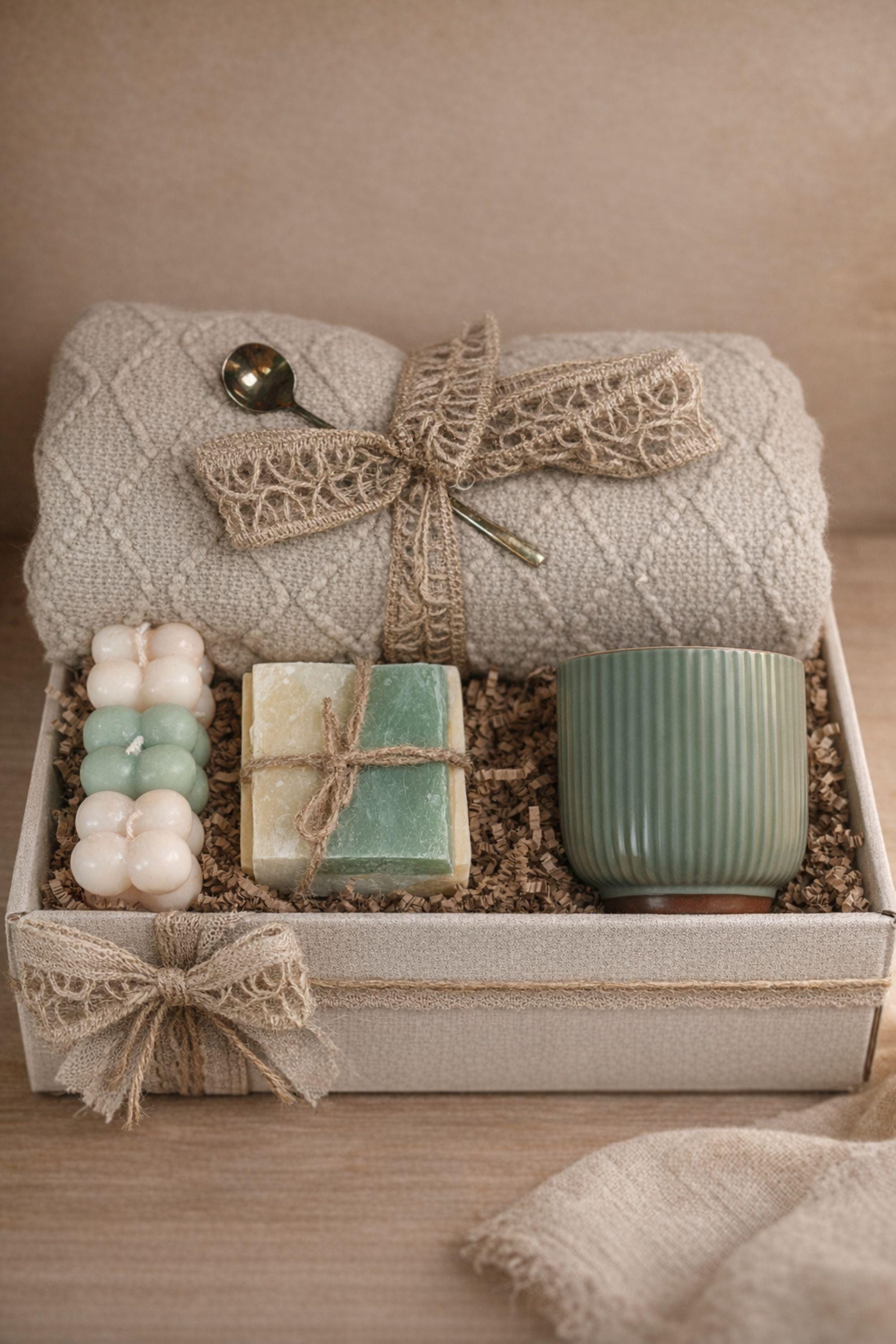 Sending You Hugs grief support gift box with sage knit blanket, ribbed green ceramic mug, handmade two-tone artisan soap, stainless steel spoon, and three bubble candles arranged inside kraft box on warm beige linen background. Sympathy care package designed for comfort during difficult times, loss support, thinking of you gift, and emotional encouragement.