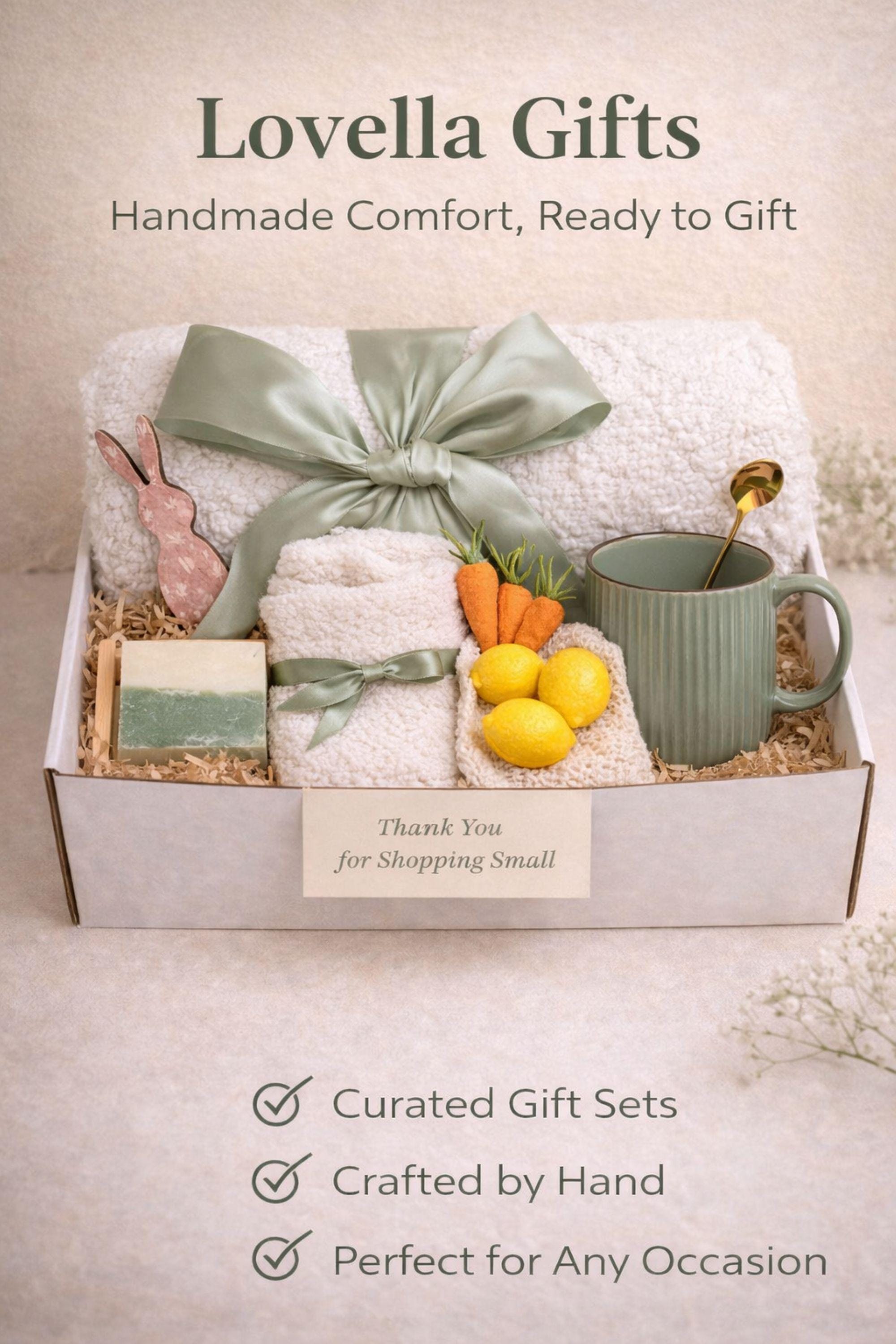 Easter gift box for women featuring a cozy knit blanket tied with green ribbon, ceramic mug with spoon, handmade artisan soap, soft socks, two lemon shaped soaps, decorative spring carrots and bunny accent arranged inside a gift box. Spring self care gift basket and Easter care package alternative to traditional Easter baskets, perfect Easter present for mom, sister, friend or women who enjoy cozy comfort gifts.