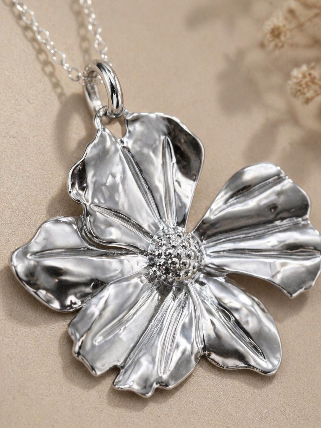Close up of silver flower necklace pendant showing polished floral details, reflective petals and elegant craftsmanship, romantic statement flower jewelry for women