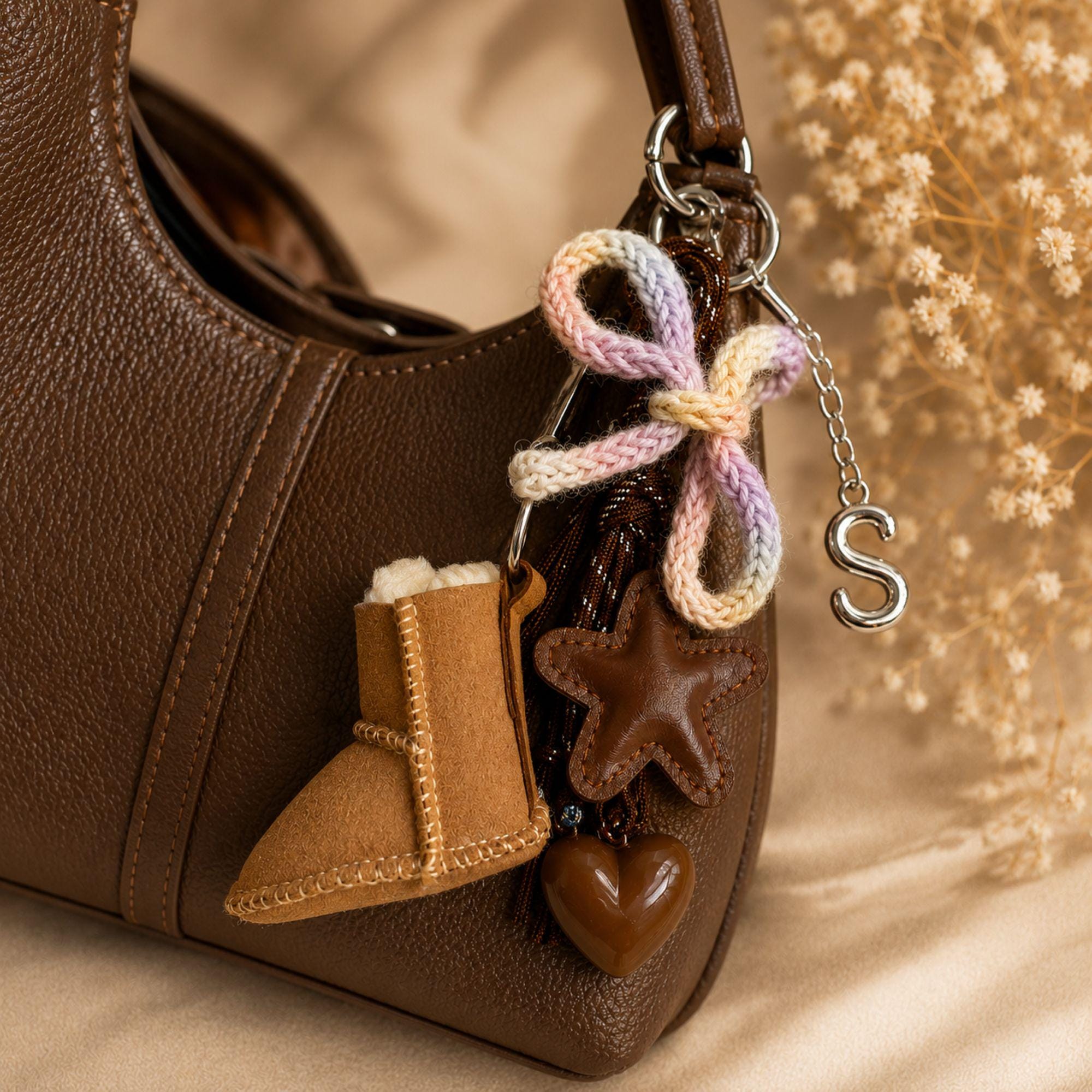 Personalized bag charm with silver initial letter, tan mini boot charm, brown leather star, glossy heart, pastel knitted bow, brown cord details and silver hardware. Cozy brown purse accessory and statement handbag charm designed for purses, totes and backpacks. Unique personalized initial keychain with layered neutral and pastel details, ideal as a cute bag accessory, backpack charm, personalized gift for her, best friend gift, sister gift or teen girl gift.